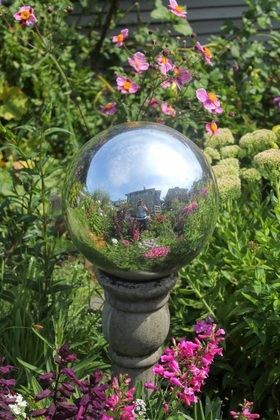 a glossy silver ball on a stone stand brings and a shiny touch to the flower bed and makes it look more personalized