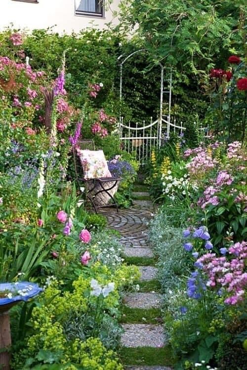 a gorgeous fairy-tale garden with bright blooms and greenery, a folding chair with a pillow and a stone path is wow