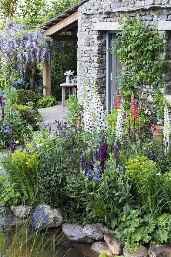 a gorgeous shady space with greenery, coral, purple, white and lilac blooms, a pond and some decor is amazing