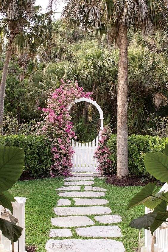 a greenery fence looks manicured and lush pink blooms climbing up the arbor add color and chic to the garden