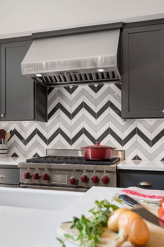 a grey and white kitchen with white countertops and a chevron tile backsplash plus stainless steel appliances