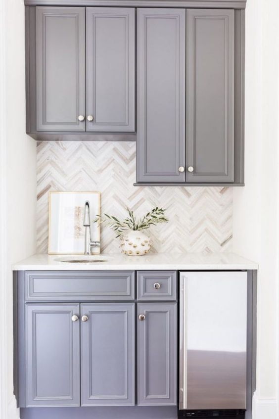 a grey kitchen with a chevron tile backsplash and white countertops is a cool and lovely space with a touch of elegance