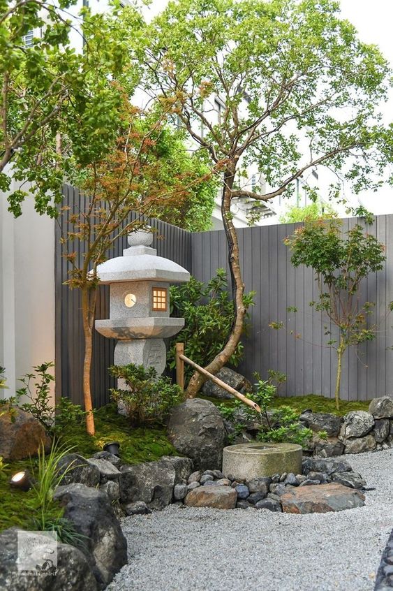 a Japanese corner garden with rocks and pebbles, moss, trees and a stone lantern plus spotlights looks very peaceful