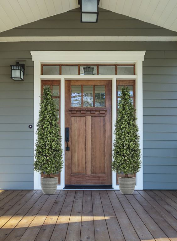 a laconic modern farmhouse porch with a stained door and glass panes covered with tall topiary trees is a chic space