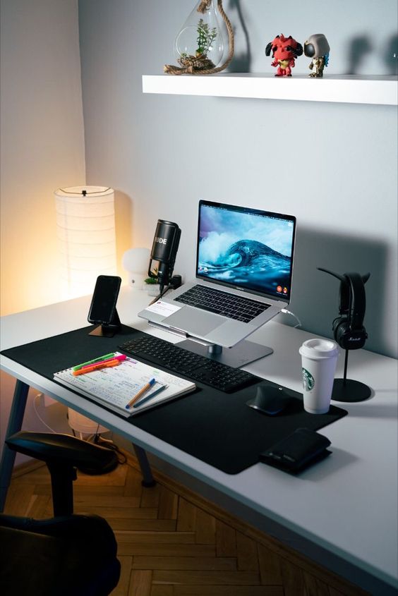 a laconic workspace with a laptop on a stand, a work zone, some devices, a lamp and some decor over the desk