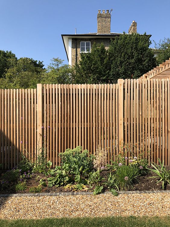 a light-stained wooden fence with a flower bed with greenery and blooms are a lovely combo for a modern garden