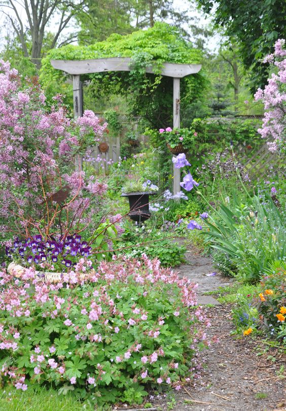 a little pastel secret garden with lots of greenery and pink, lilac and purple blooms plus an urn with flowers feels very beautiful