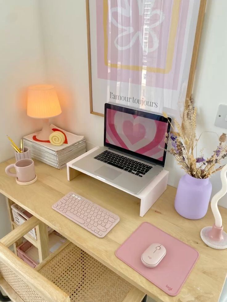 a little pastel workspace with a desk and a cane chair, a stand with a laptop, lilc and dusty pink accessories and an artwork is very cute