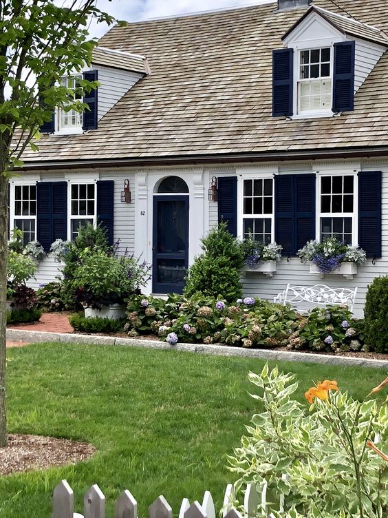 Long beds with blooms and greenery and potted plants create a lovely cottage front yard that perfectly matches the exterior of the house. 