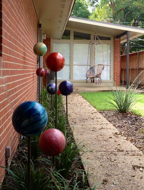 a long green garden bed accented with bright gazing balls on stand that remind of the Solar system