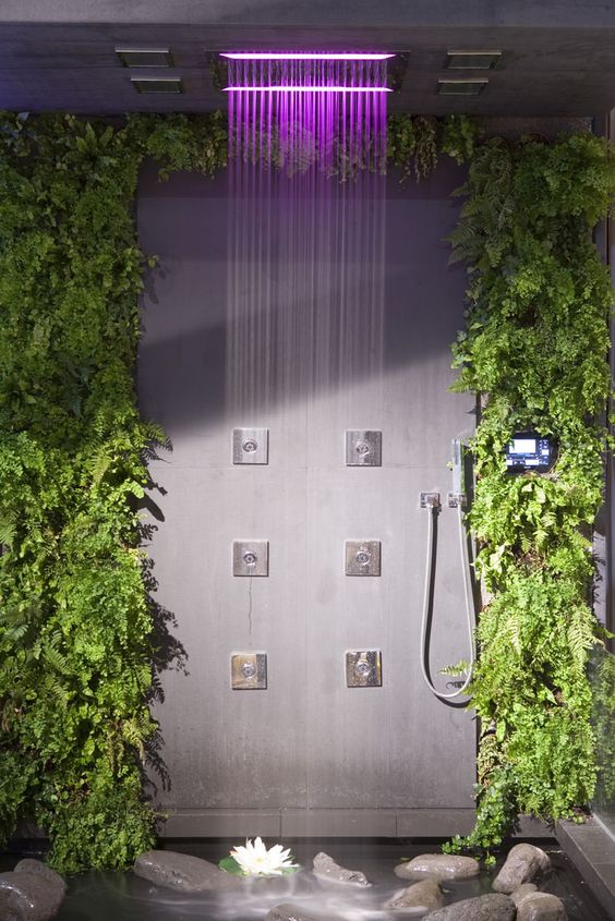 a lovely contemporary shower space with living walls, rocks on the floor and rain shower heads with colored lights