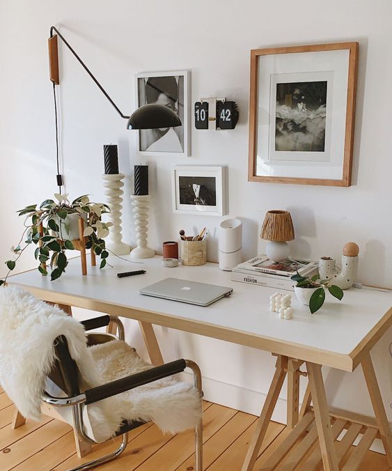 a lovely modern workspace with a trestle desk, a gallery wall, chic decor, candles and lamps and a black chair