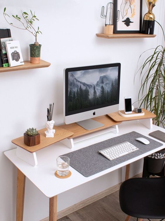 a minimal workspace with a desk and a stand with a monitor plus decor, little shelves with decorations and a black chair