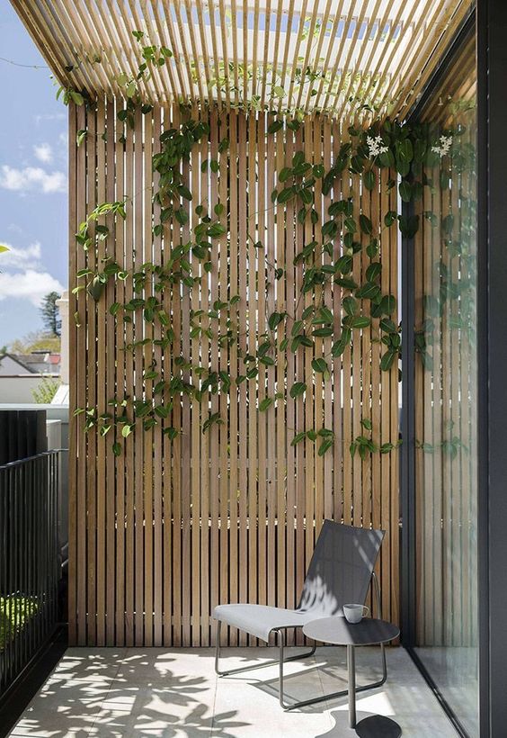 a minimalist balcony with a chair, a side table and a trellis and greenery climbing up is a cool space if you love minimal decor