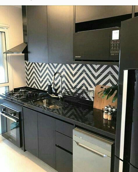 a modern black kitchen with a black and white chevron tile backsplash and some built-in appliances is laconic yet bold