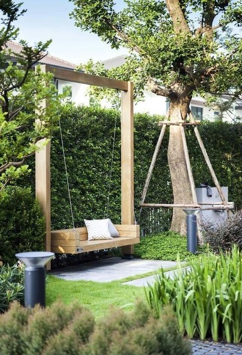 a modern deck with a frame and a minimal swing, a side table and some greenery, trees and a living wall around the space