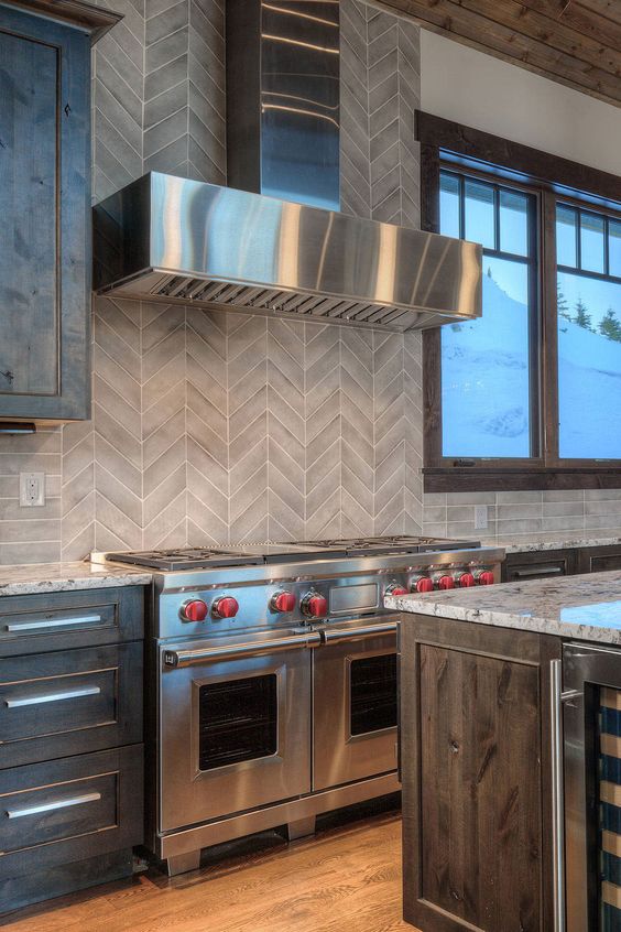 a modern farmhouse kitchen with dark-stained cabinets, stone countertops and a chevron tile backsplash plus stainless steel appliances