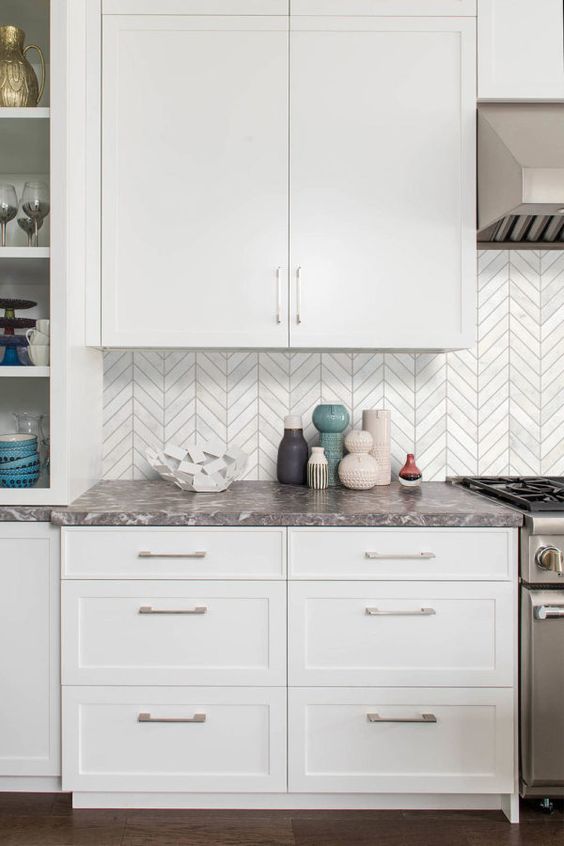 a modern farmhouse kitchen with white cabinets, grey stone countertops and a white chevron backsplash plus stainless steel appliances