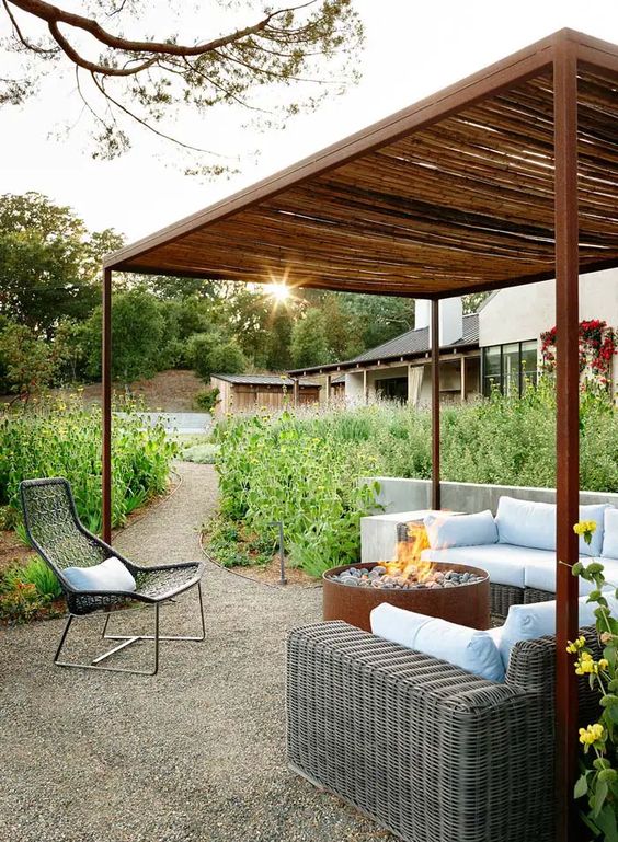 a modern gazebo with a gravel floor, a wicker sofa with pillows, a fire pit and a black wicker chair is a lovely and cozy space