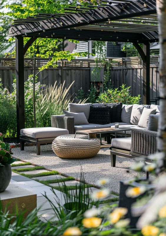 a modern gazebo with a grey outdoor sofa, a jute pouf and some seating furniture and grasses and greenery around