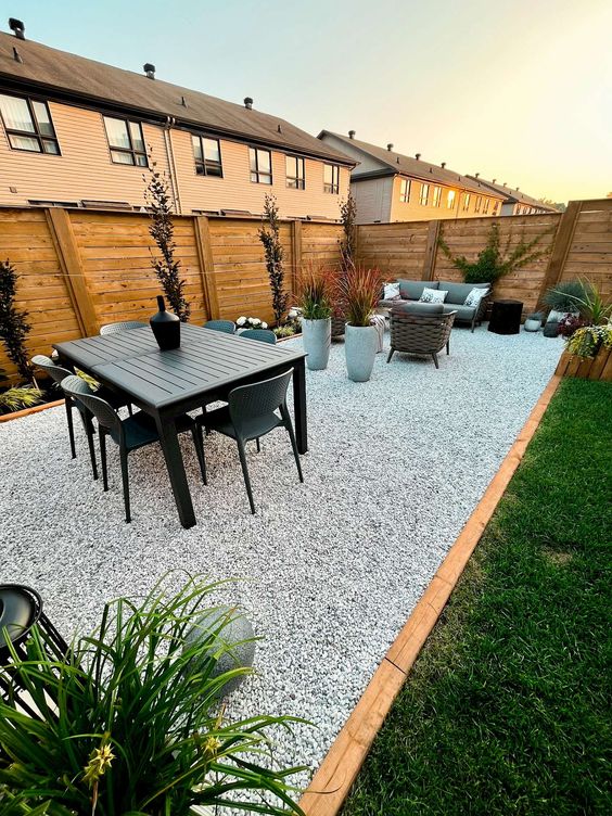 a modern gravel patio with a dining zone with modern dark furniture, a living room with a sofa and stools, potted plants around