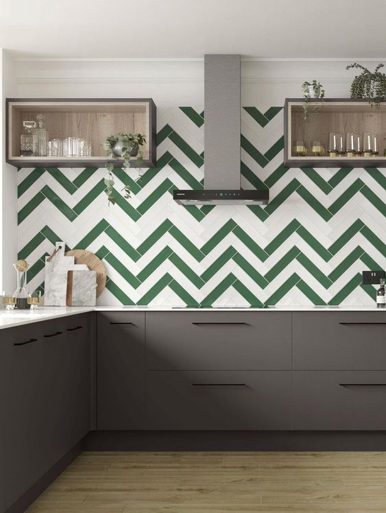 a modern grey kitchen with a green and white chevron tile backsplash, open box shelves and stainless steel appliances