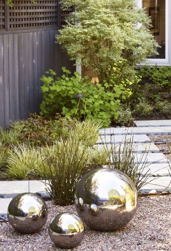 a modern landscape with greenery, a concrete path and a gravel yard plus mirror balls on the ground for a catchy and glossy touch