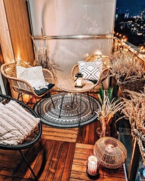 a modern meets boho balcony with rattan furniture, a cane coffee table, various grasses in baskets and vases, candle lanterns and lights