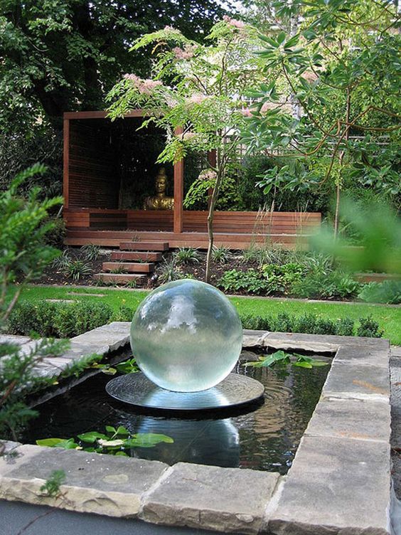 a modern pond clad with stone, with some plants and a glass sphere in the center for a bold accent