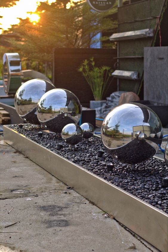 a modern raised garden bed with black pebbles inside and mirror gazing balls lifted up the bed