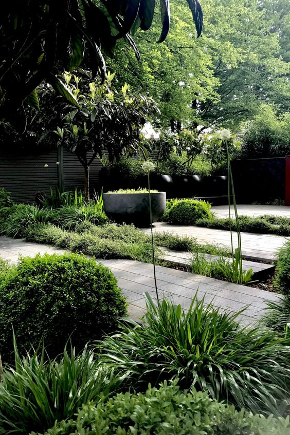 a modern garden with wooden decks, some greenery, shrubs and trees plus a large planter with greenery is adorable