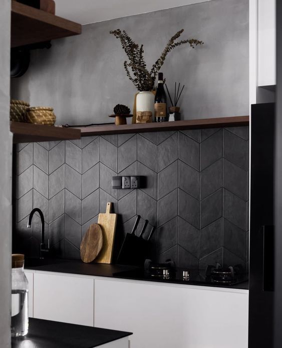 a modern white kitchen with black countertops, a black chevron tile backsplash and some open shelves is adorable