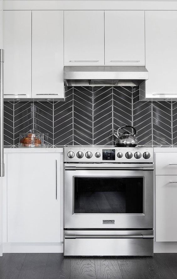 a modern white kitchen with white countertops, a graphite grey chevron tiles on the backsplash and stainless steel appliances