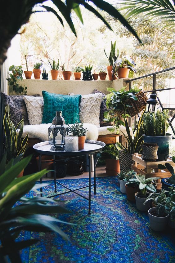 a Morocco-inspired balcony with a bold blue rug, a loveseat with boho pillows, a side table, potted plants and cacti, Moroccan lanterns