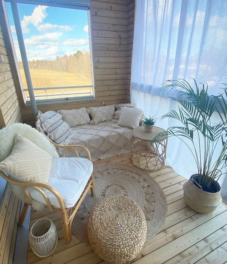 a neutral boho balcony with a sofa with pillows, a rattan chair, a jute rug and a pouf, potted plants and candle lanterns is a stylish idea