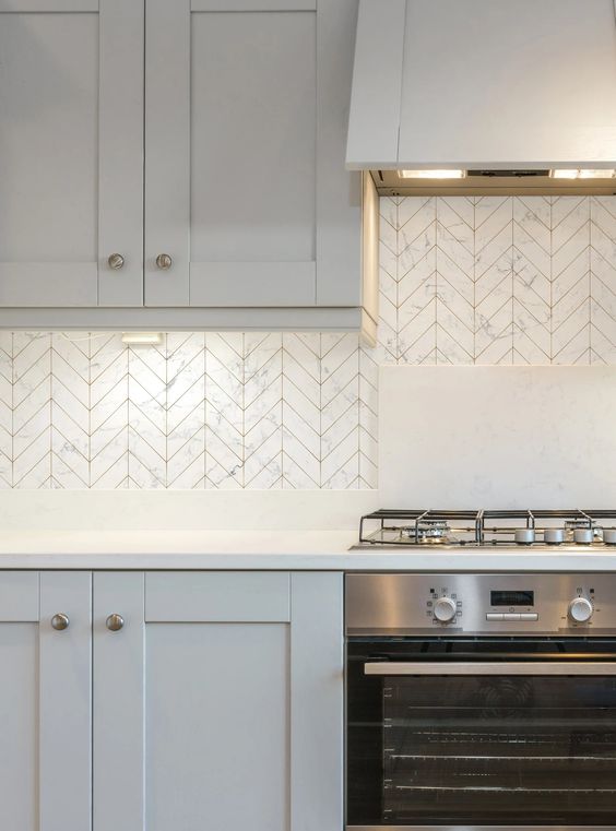 a pale grey kitchen with white countertops and a white marble tile backsplash plus stainless steel appliances