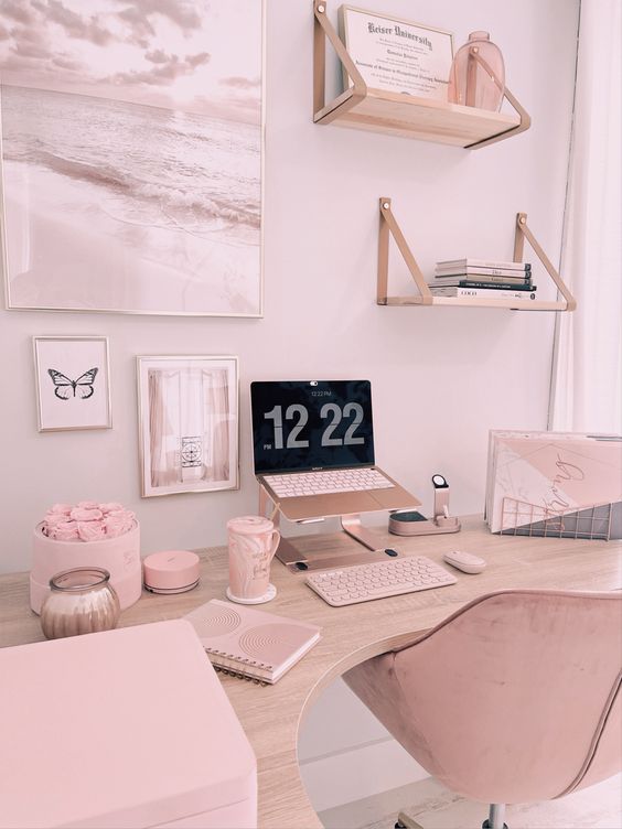 a pastel pink working space with a laptop on a stand, hanging shelves with books, some accessories and even some roses in a box