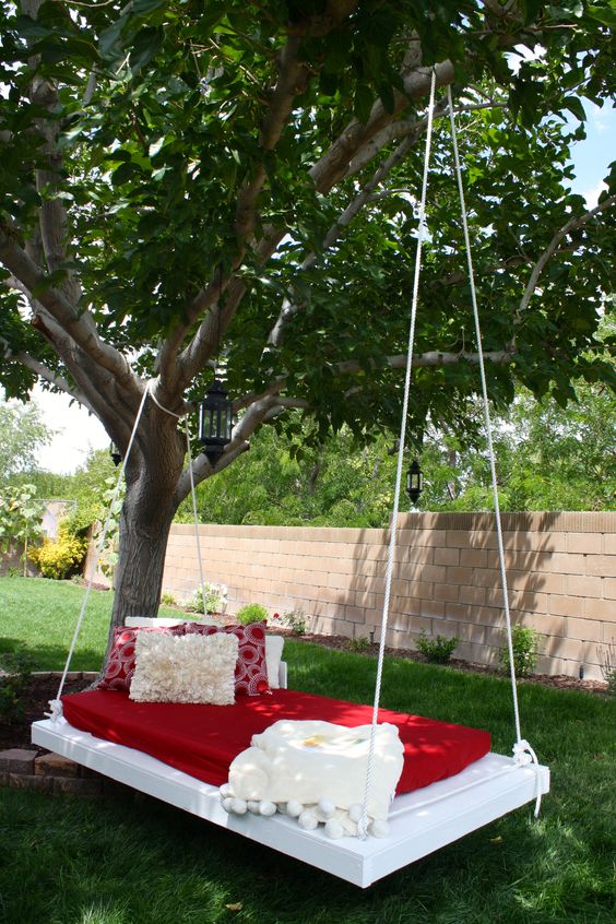 a hanging daybed on the tree, with red and white bedding, is a super cool piece to sleep outdoors