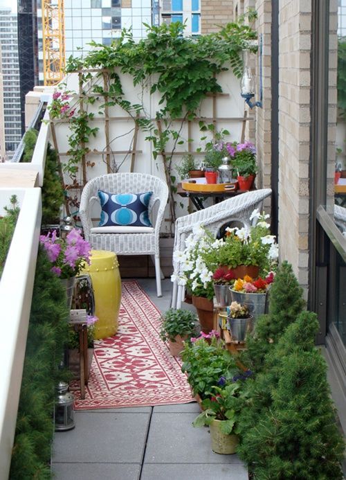 a pretty little balcony with white wicker chairs and side tables, greenery and blooms in pots and buckets and a small trellis with greenery