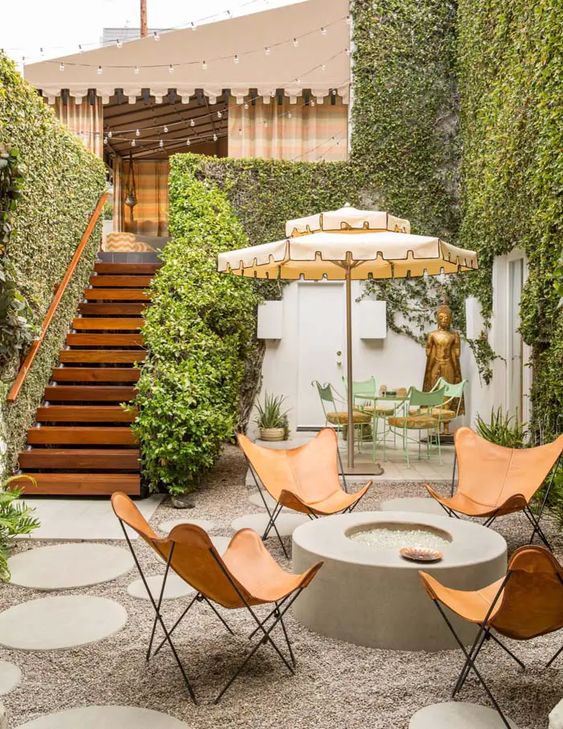 a pretty modern gravel patio with a fire put, leather butterfly chairs, a dining zone with green chairs and an umbrella