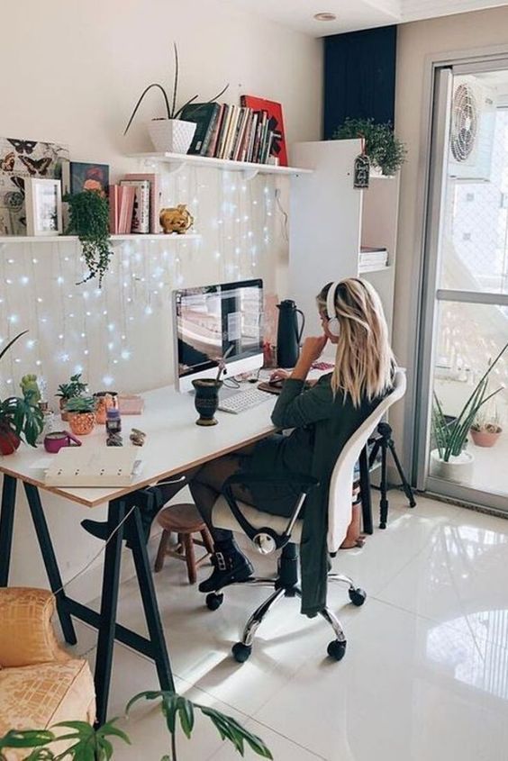 a pretty modern workspace with a trestle desk, a white chair, some shelves with lights, potted plants and lights hanging down