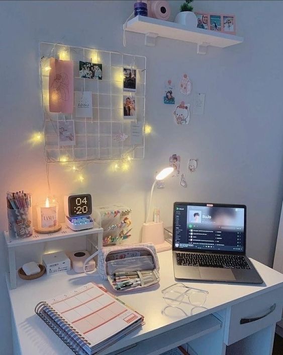 a pretty small workspace with a gird with memos and lights, a shelf, a stand with various decor, a laptop and some stuff