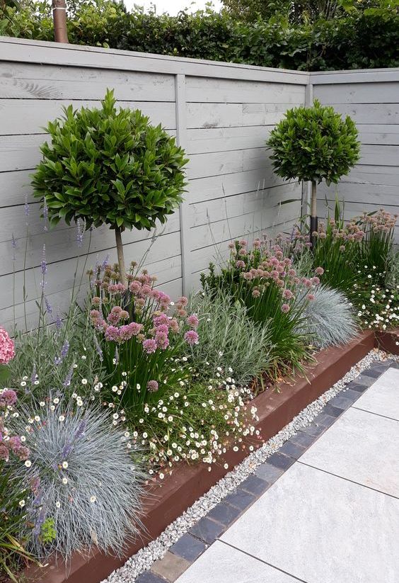 a raised flower bed as a corner garden with blooms, greenery and topiary trees is amazing to refresh a backyard