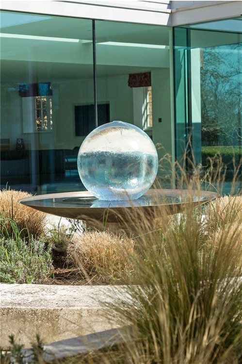 a raised garden bed with grasses and a metal bowl with a gazing ball is a lovely decoration for outdoors