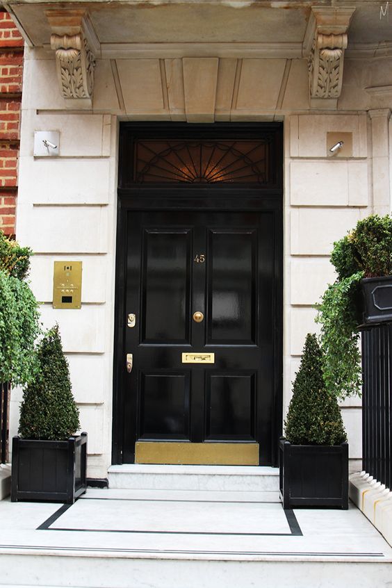 a refined and laconic front porch with a black door, topiaries and greenery in pots is a super chic space