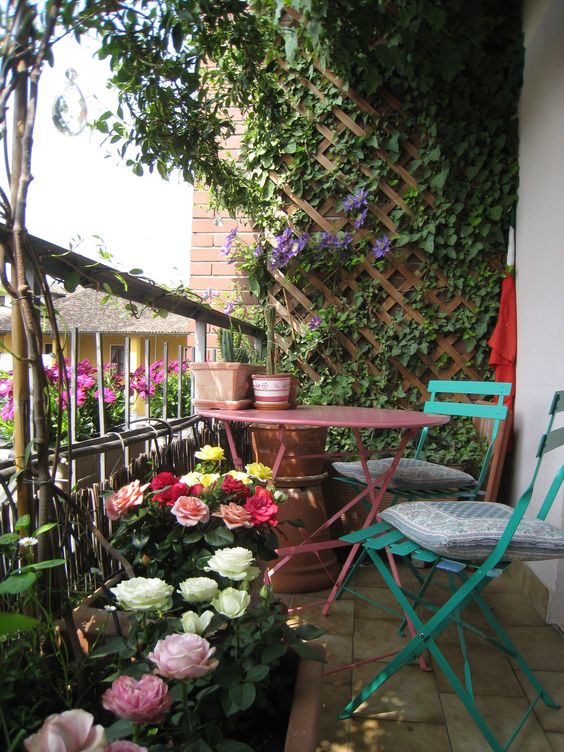 a refined balcony with a trellis on the wall and greenery, blooms in planters, some bright folding furniture is cool