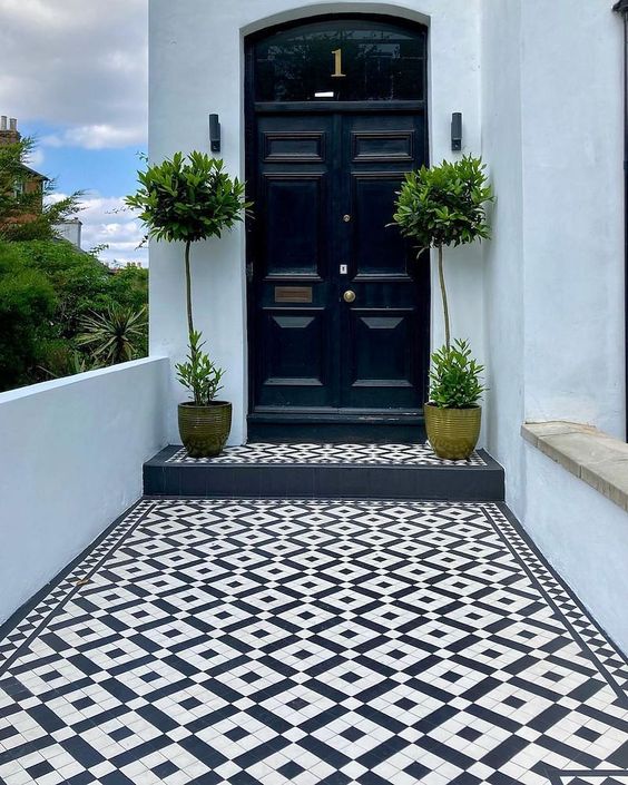 a refined minimal porch with a black door, topiaries and a black and white checked floor is a super chic space