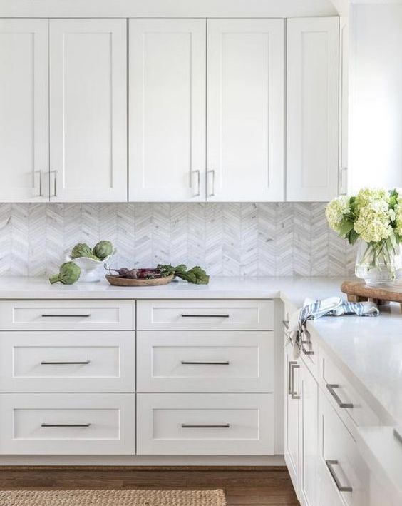 a refined white kitchen with shaker cabinets, a white marble chevron backsplash and stainless steel fixtures