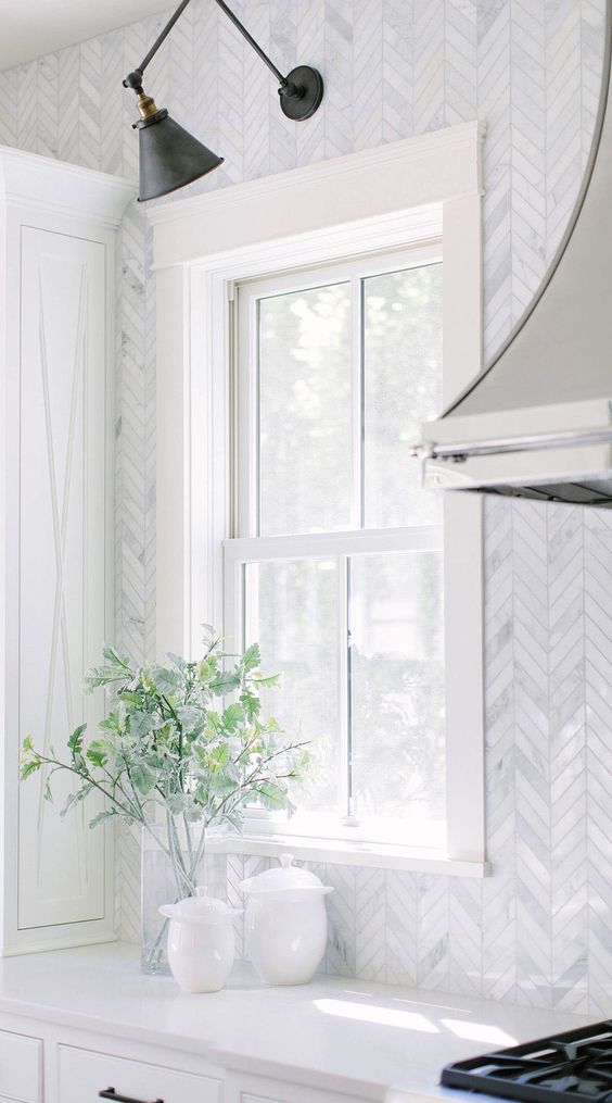 a refined white kitchen with white countertops, a white marble chevron backsplash, black touches for a bit of contrast in the space