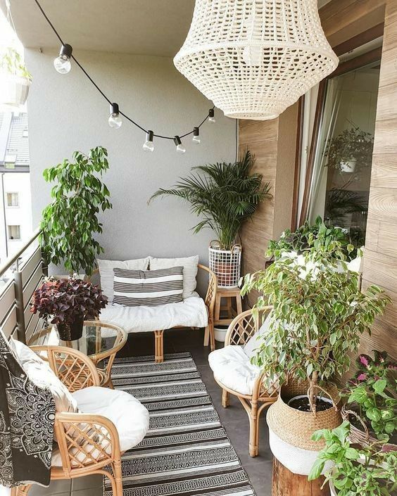 a relaxed neutral boho rug with rattan furniture, neutral upholstery, potted greenery, a chandelier and some bulbs hanging over the space